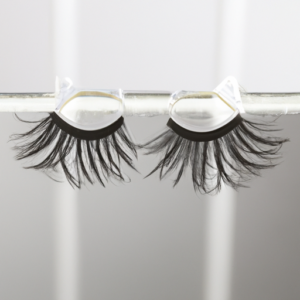 A pair of false eyelashes with a magnet attached to each end, hovering over a metallic surface.