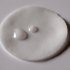 A close-up of a white cotton pad with a few drops of makeup remover on it.
