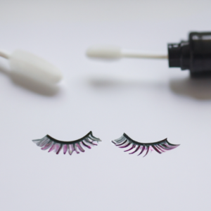 A pair of eyelashes with a bottle of mascara and a cotton swab.